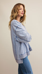 A woman modeling a light blue, long-sleeved sweatshirt with visible dark blue stitching and blue jeans.