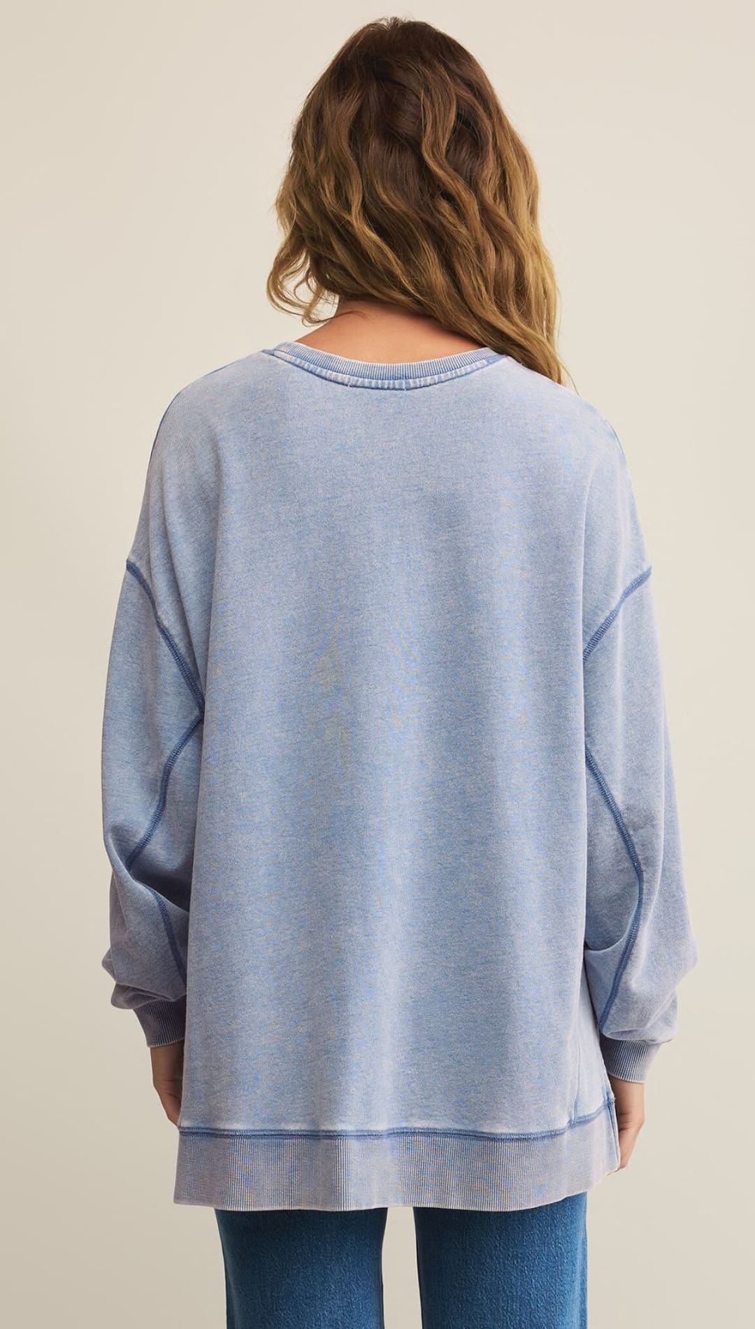 A woman in a long-sleeved, light blue, oversized sweatshirt with visible seams and a ribbed hem and cuffs.