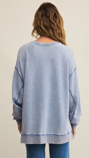 A woman in a long-sleeved, light blue, oversized sweatshirt with visible seams and a ribbed hem and cuffs.