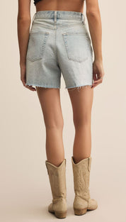 Light wash denim shorts with frayed hems paired with tall beige cowboy boots.