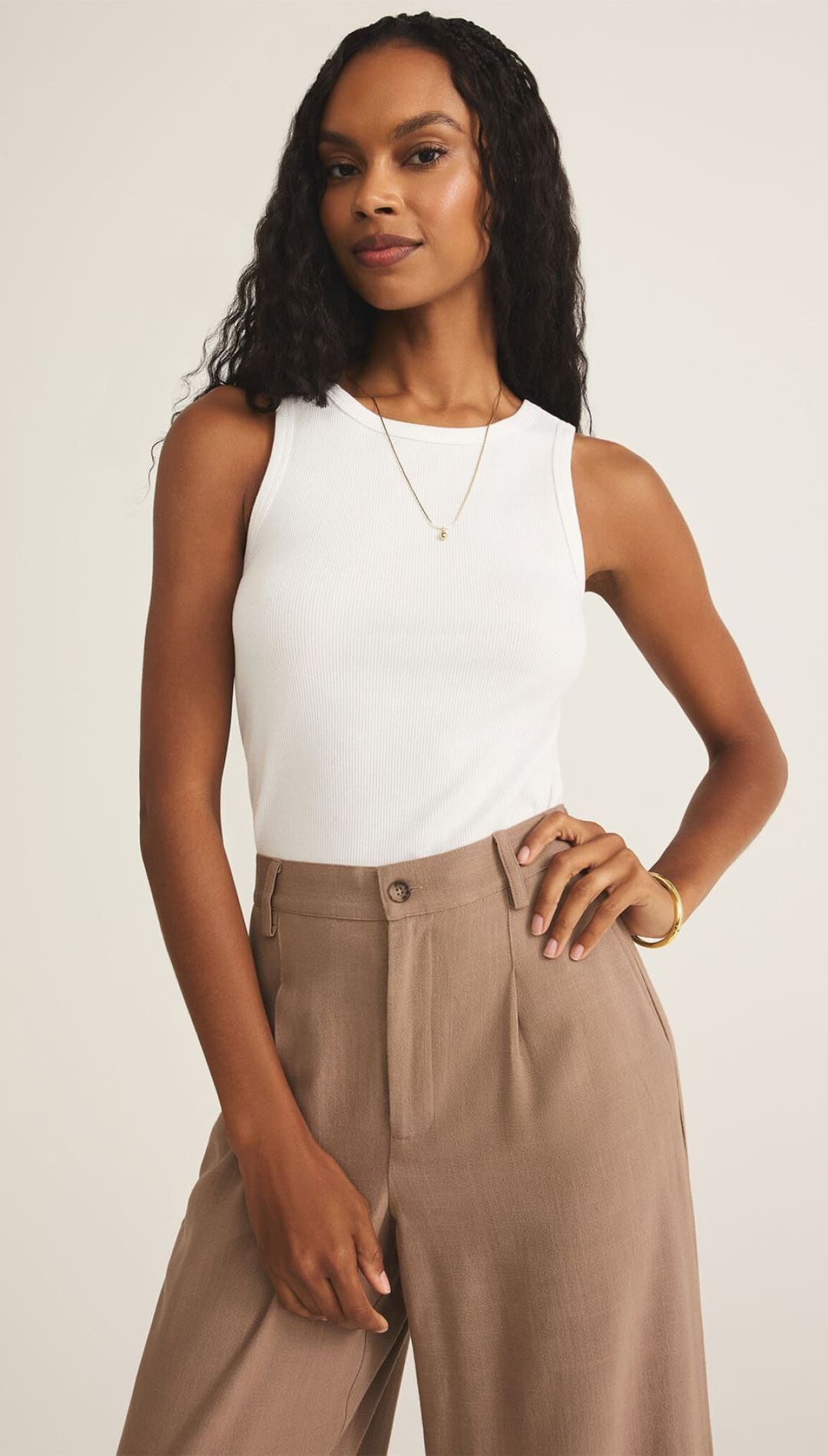 A woman models a white sleeveless ribbed tank top and wide-leg brown pleated trousers.