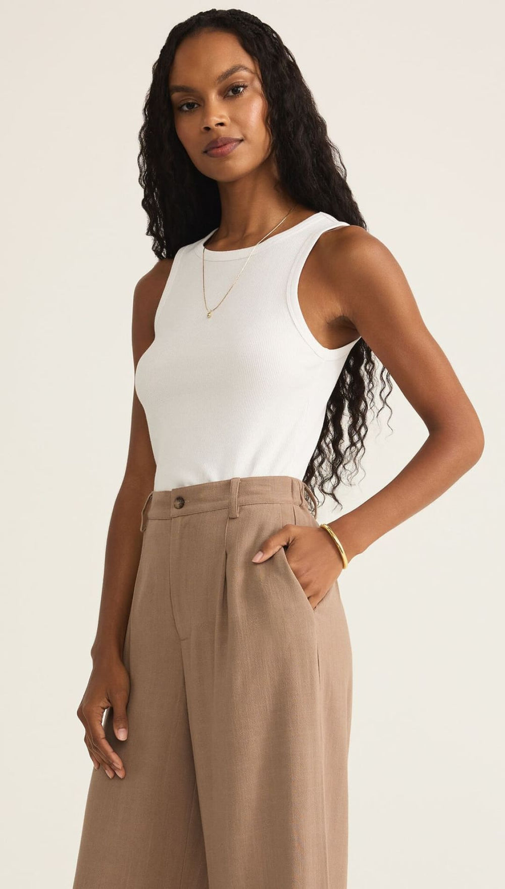 A woman wearing a white sleeveless top and brown wide-leg pants.